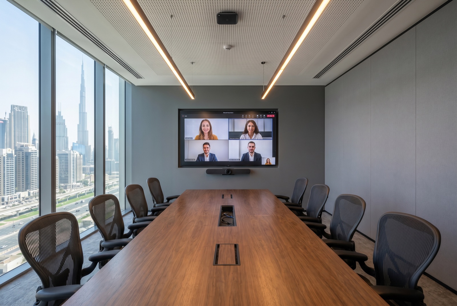 Executive twelve-seat boardroom in a Dubai commercial tower with walnut-veneer table, Herman Miller chairs, Logitech Rally Bar Pro and wall-mounted Microsoft Teams Rooms display overlooking the Burj Khalifa